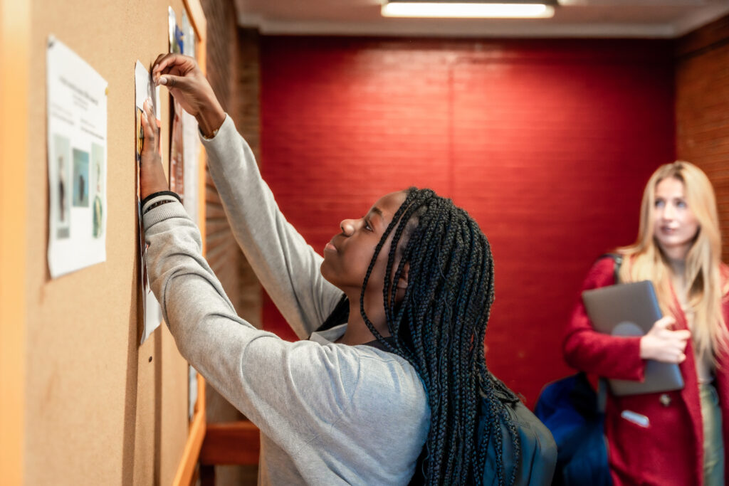 Young student putting up a notice on university bulletin board - Global Solution Services