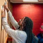 Young student putting up a notice on university bulletin board - Global Solution Services